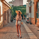 Attractive girl tourist in sunglasses, a blouse and a straw hat is walking along the alleys of the city. The concept of tourism, travel, leisure.